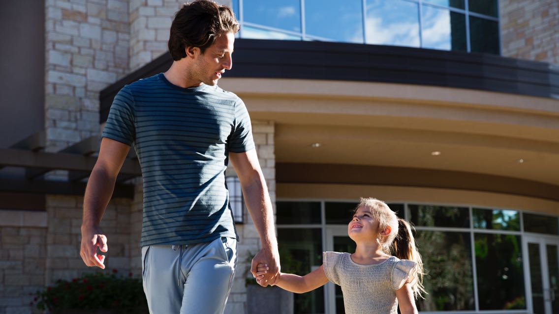 A father and daughter hold hands and smile at each other